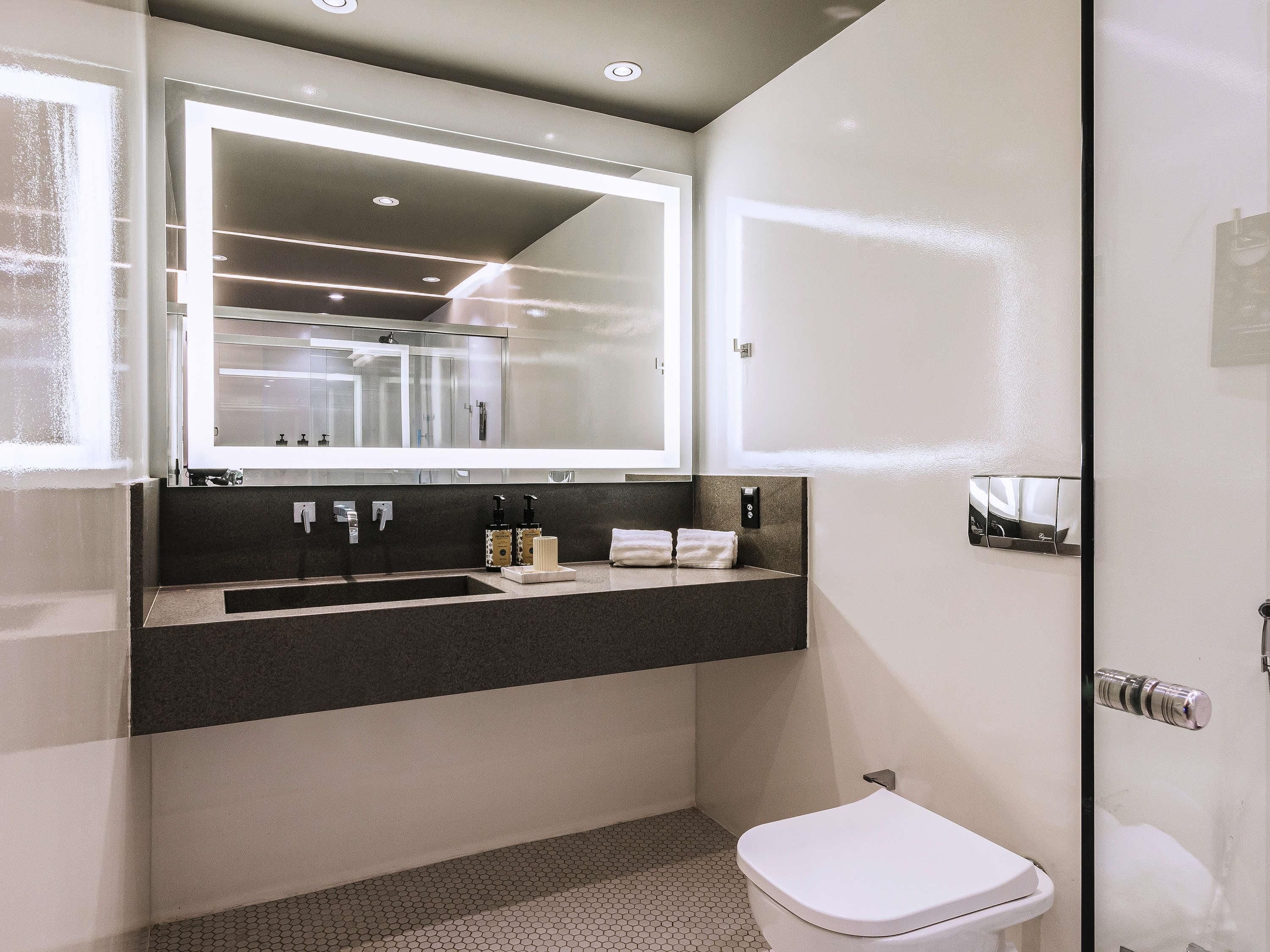 A modern bathroom with a large mirror, a sink, and a toilet.
