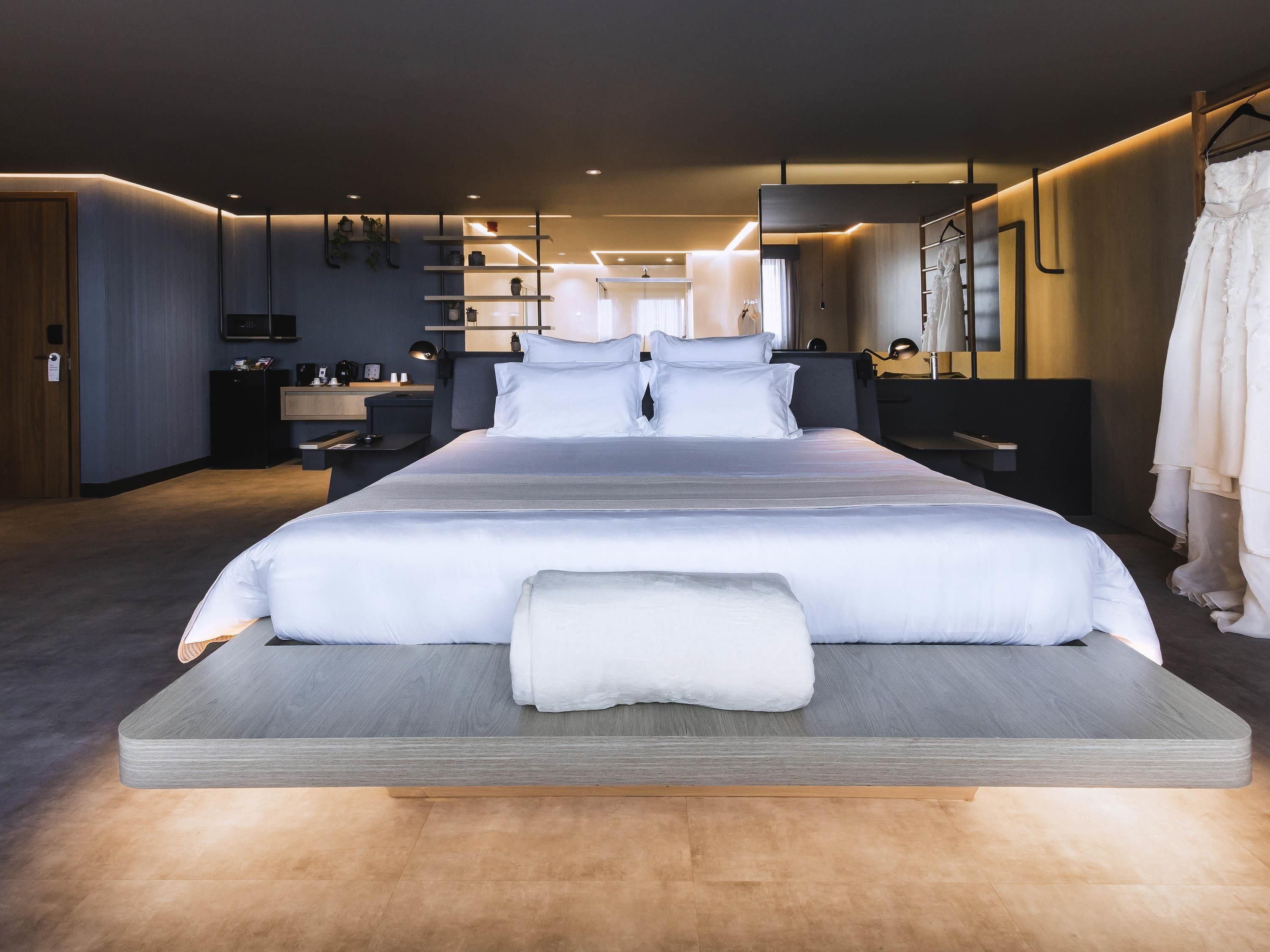 A modern hotel bedroom with a large bed, bedside tables, a wardrobe, and a mirror.