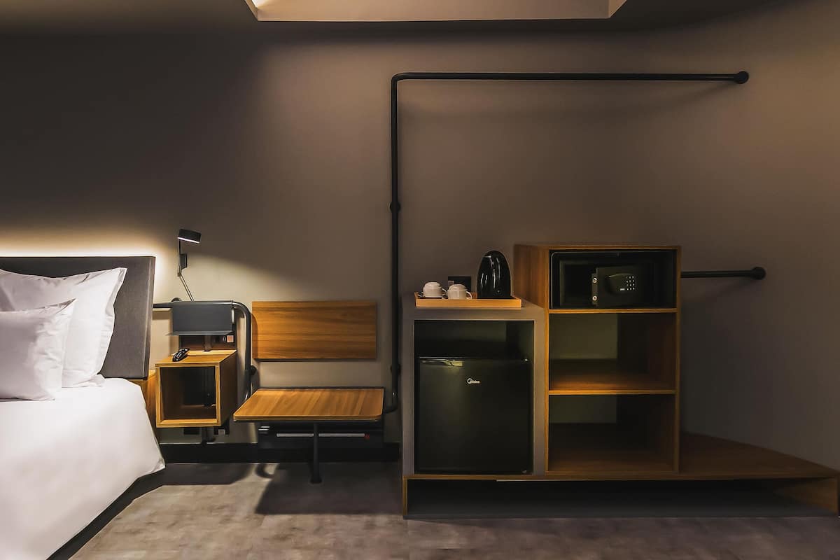 Ein kleines Hotelzimmer mit Bett, Nachttisch, Lampe, kleinem Holztisch, Mikrowelle und einer Schrankwand.