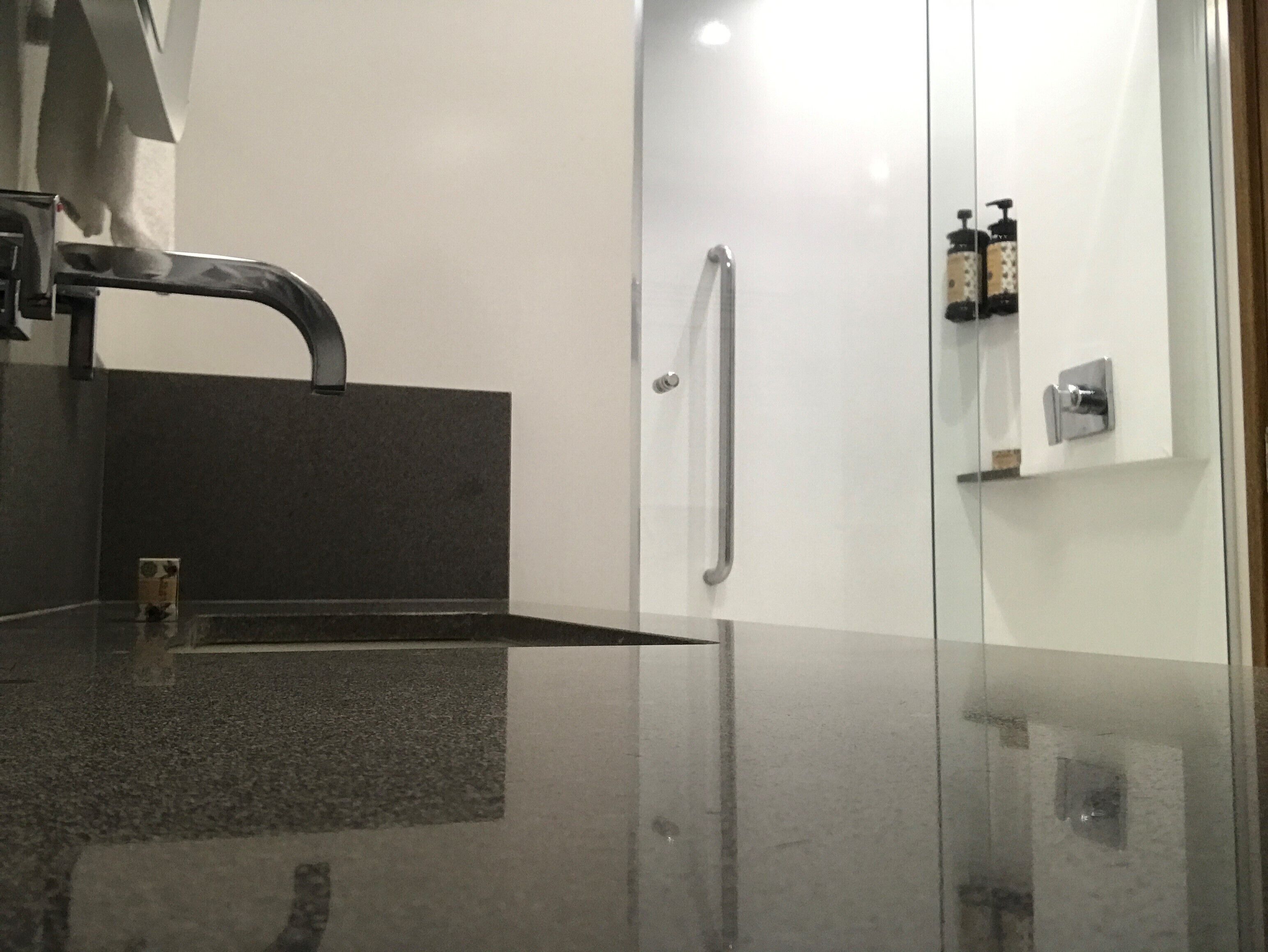 Ein modernes Badezimmer mit einer dunklen Granittafel, einem einzelnen Wasserhahn, einer Duschkabine aus Glas und einer kleinen Seifenspenderflasche an der Wand.