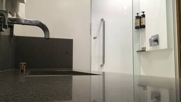 Ein modernes Badezimmer mit einer dunklen Granittafel, einem einzelnen Wasserhahn, einer Duschkabine aus Glas und einer kleinen Seifenspenderflasche an der Wand.