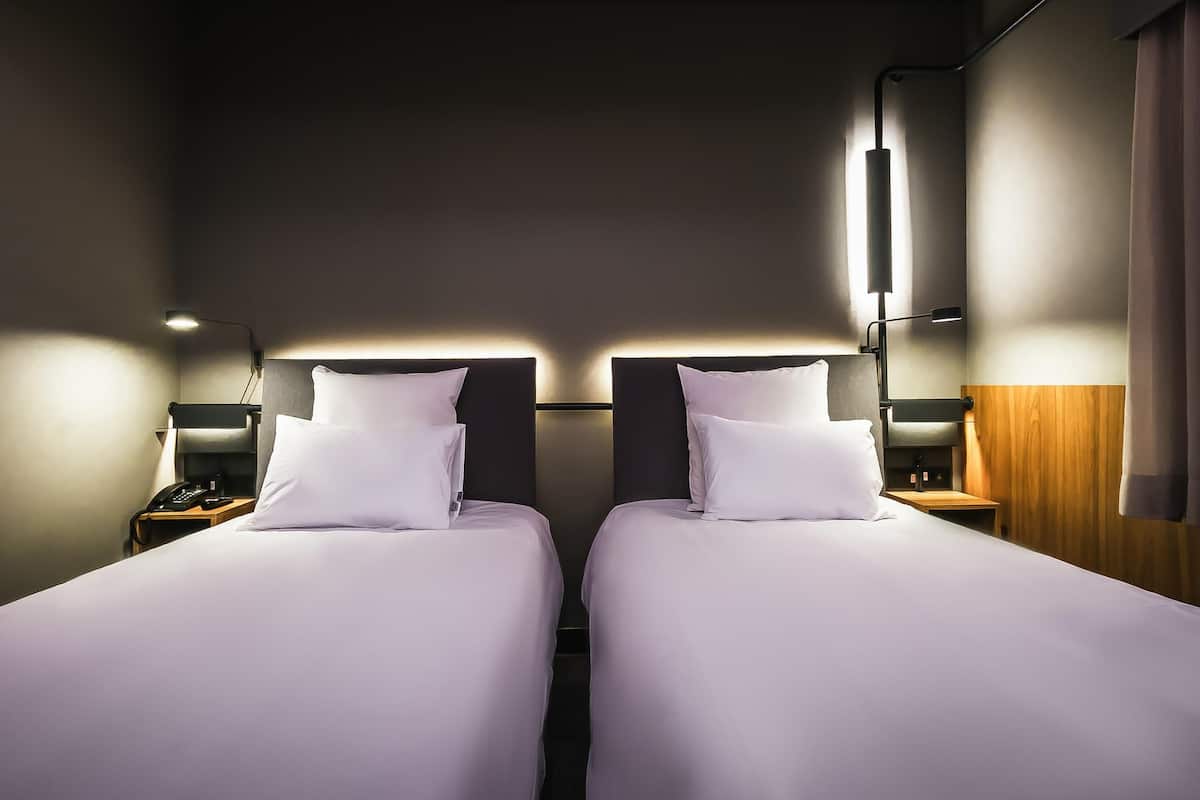 Ein Hotelzimmer mit zwei Betten, Nachttischen, Lampen und einer Wand im Holzdesign.