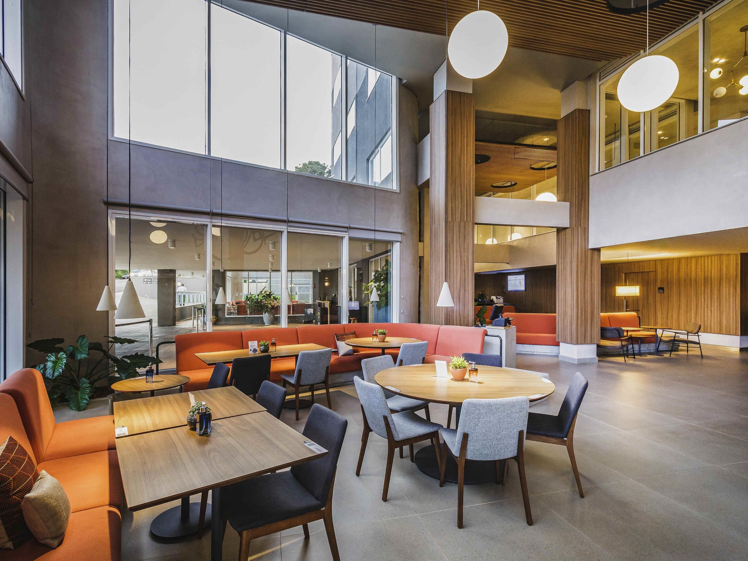 A spacious lobby with high ceilings, large windows, and modern furniture including sofas, tables, and chairs.