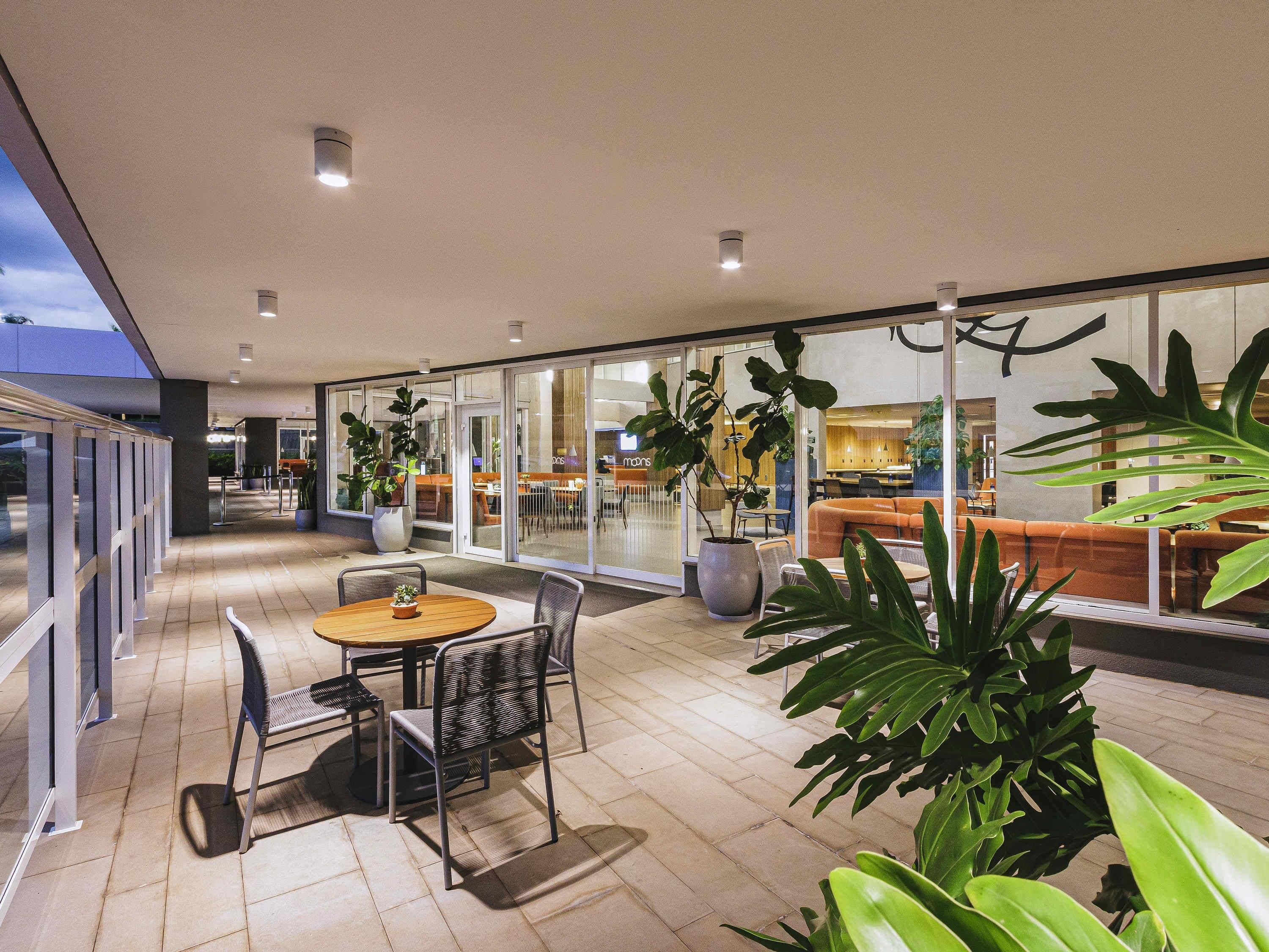 An indoor patio area with a round table and chairs, potted plants, and a seating area with orange cushions.