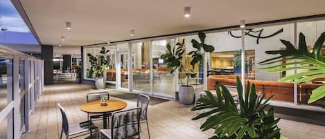 Un patio interior con una mesa redonda y sillas, plantas en macetas y un rincón de descanso con cojines anaranjados.