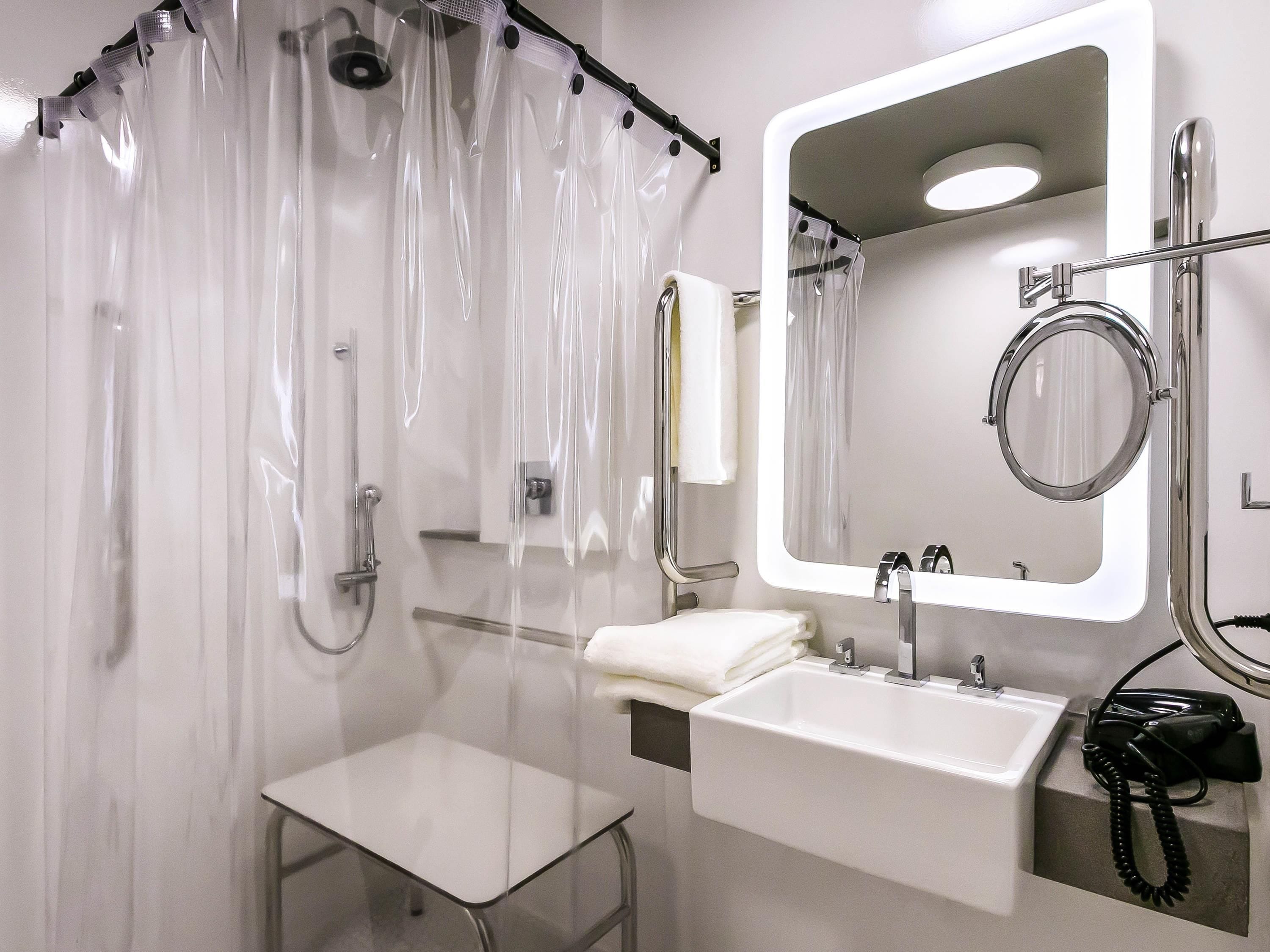 A modern bathroom with a glass shower enclosure, a white sink, and a mirror with a round frame.