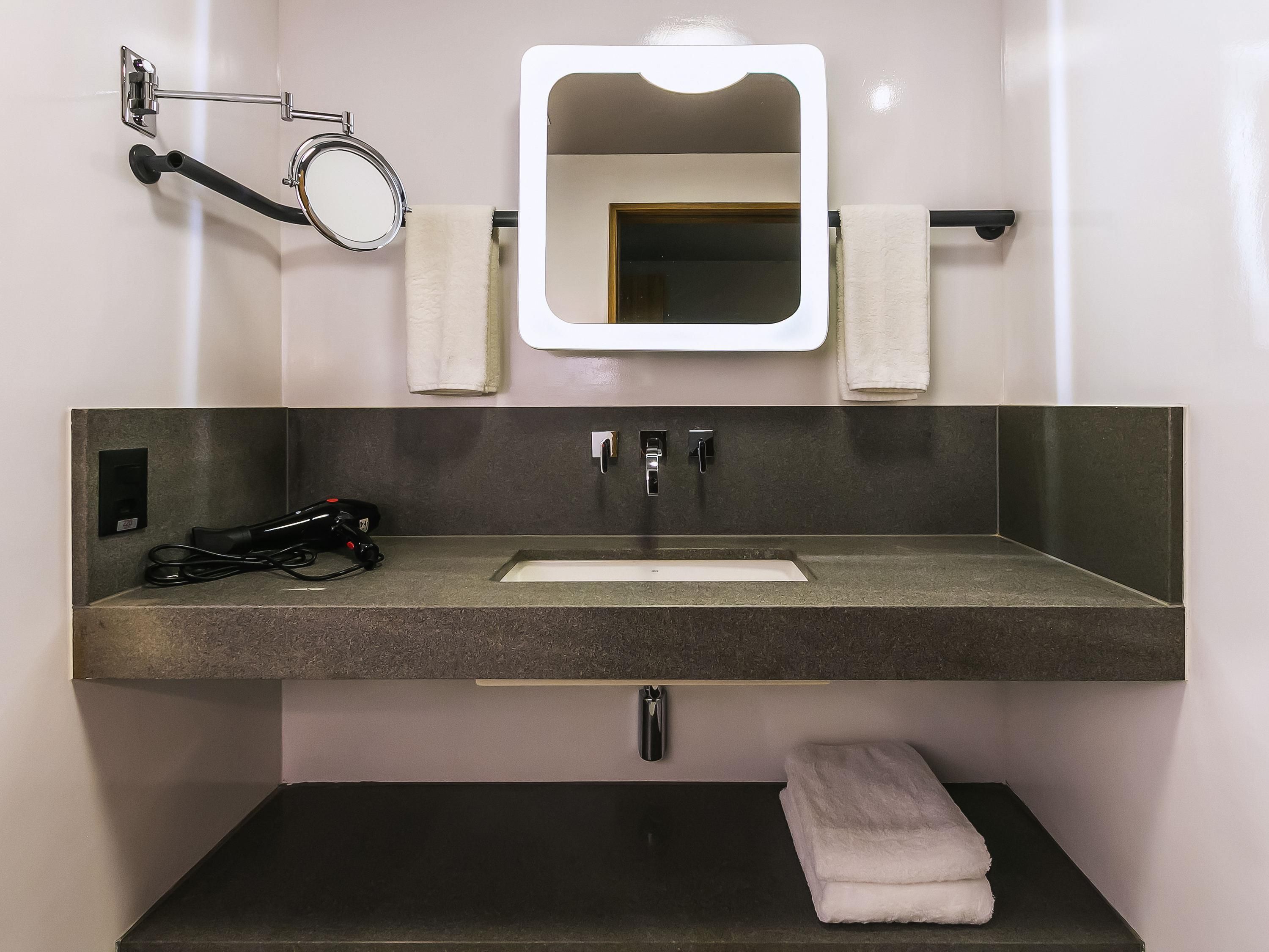 A bathroom with a rectangular sink, a mirror, two towel racks, and a towel on the counter.