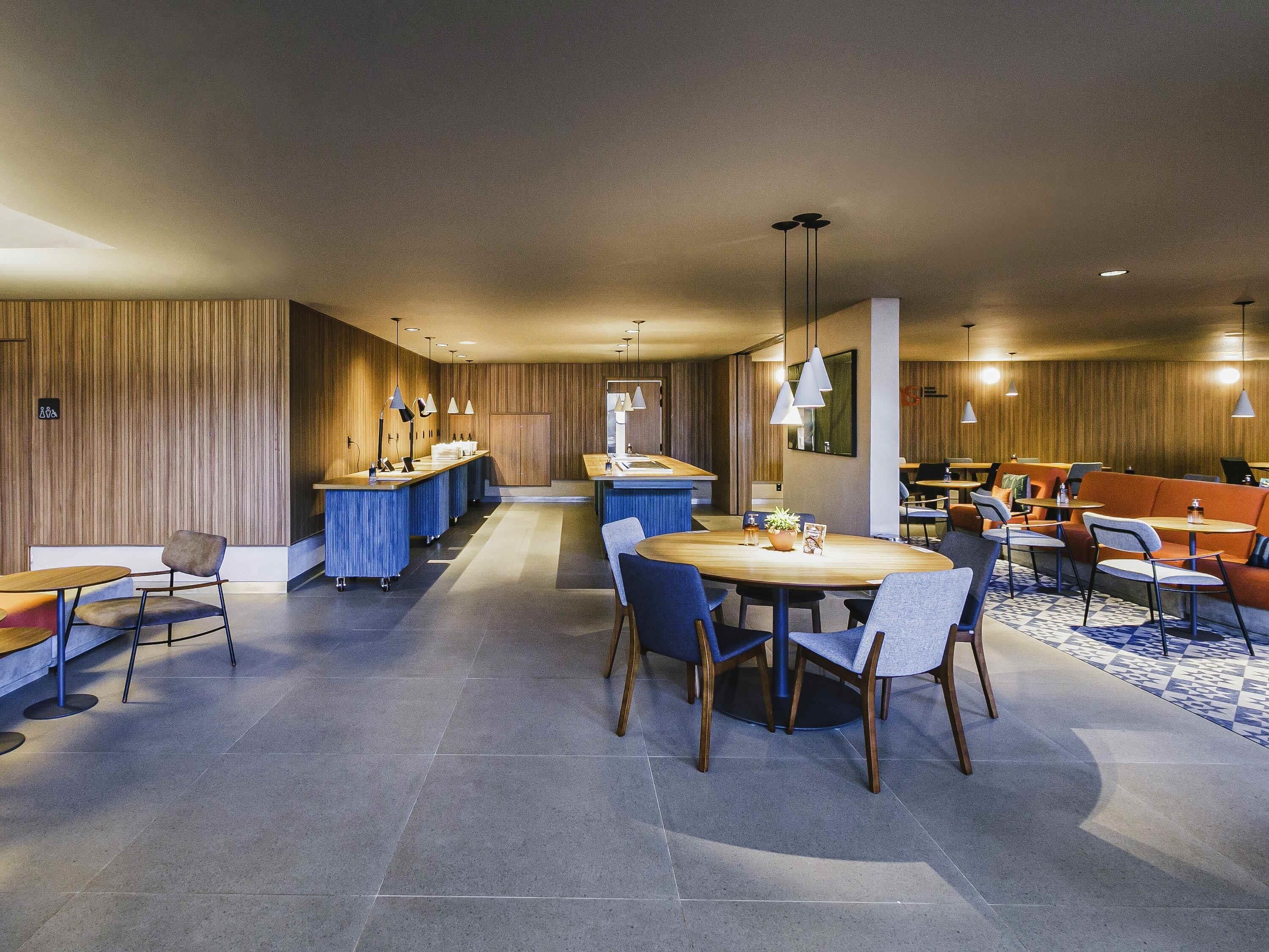 Un moderno vestíbulo de hotel con una zona de comedor central, un bar y diferentes disposiciones de asientos.