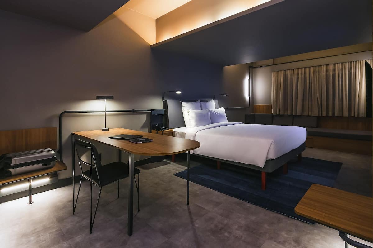Ein Hotelzimmer mit Bett, Nachttisch, Schreibtisch, Stuhl und einer Schreibtischlampe.