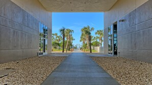 A modern building with a concrete exterior, a central pathway, and palm trees in the background.