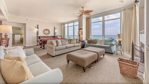 A spacious living room with a large window overlooking the ocean, a fireplace, and a pool table.