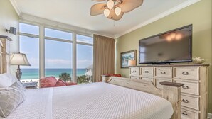 A hotel room with a large bed, a television, a dresser, and a view of the ocean.