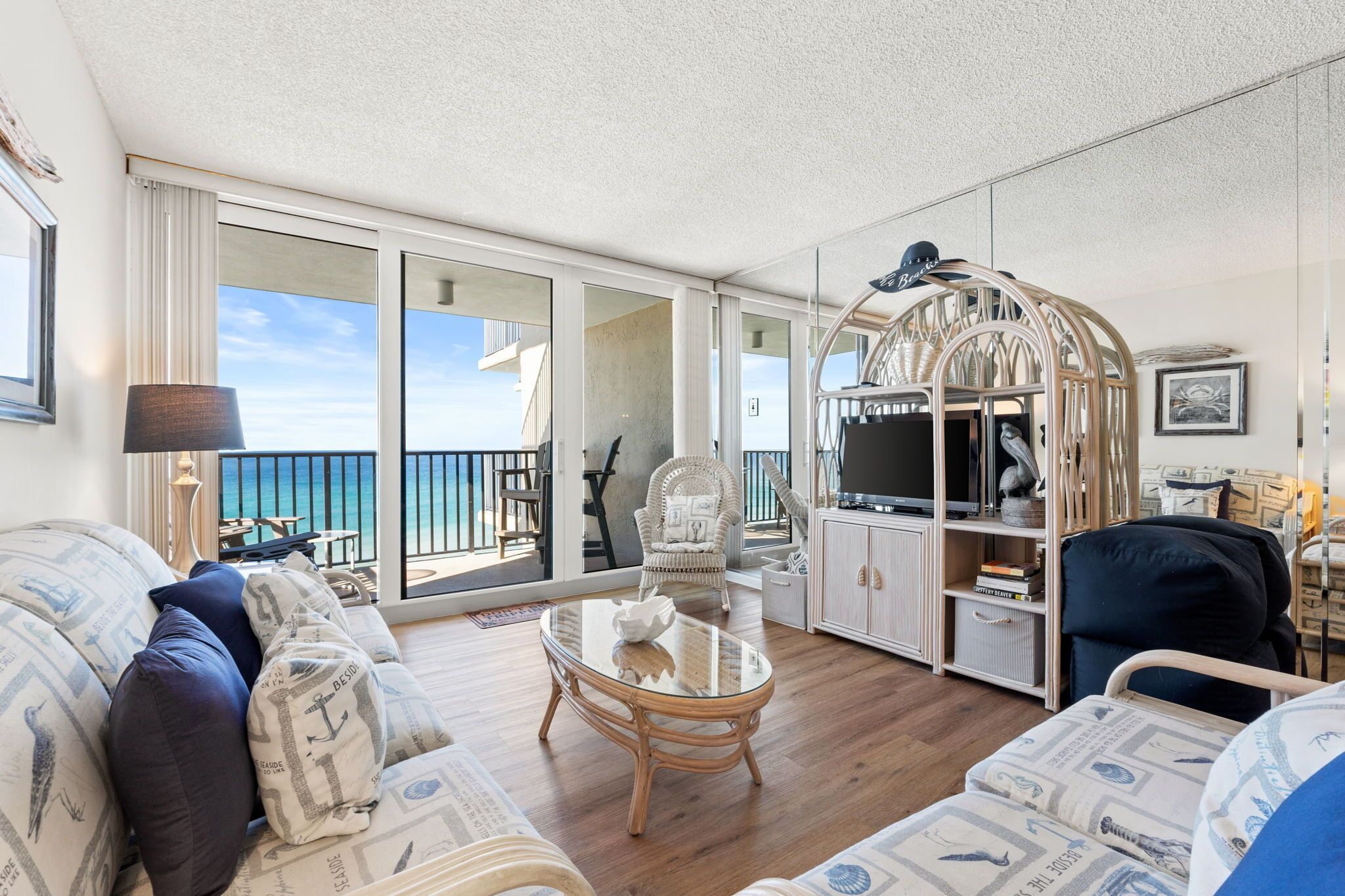 A spacious living room with a large window, a wicker chair, a glass coffee table, and a television.