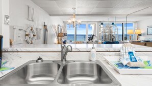 Een moderne keuken met een groot schiereiland, roestvrijstalen spoelbakken en uitzicht op de oceaan door grote ramen.
