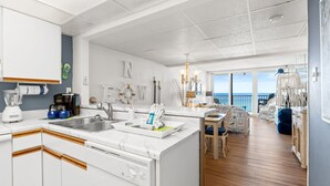 Een moderne keuken met witte kasten, een ingebouwde vaatwasser en een groot keukenblok met een spoelbak. Er is een eethoek met uitzicht op de oceaan.