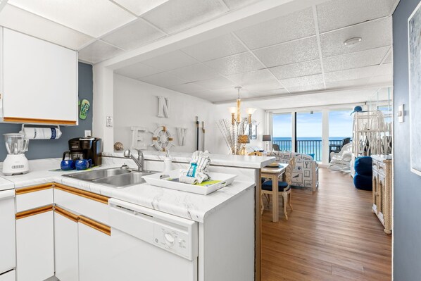 Una cucina moderna con mobili bianchi, lavastoviglie integrata e una grande isola con lavello. C'è un'area pranzo con vista sull'oceano.