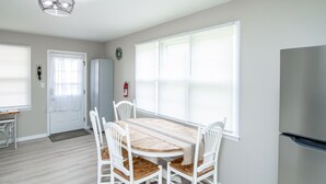 Eine kleine Küche mit Esstisch, Stühlen, einem Kühlschrank und einem Fenster mit Jalousien.