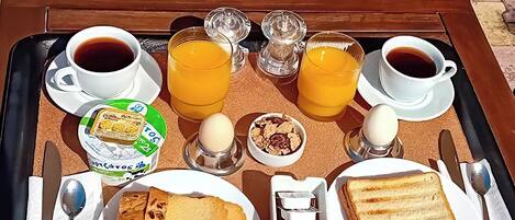 Ein Frühstücksbrett mit Kaffee, Orangensaft, Toast, Marmelade und einem Joghurtbecher.