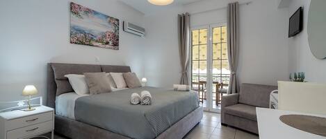 Une chambre à coucher comprenant un lit, des tables de chevet, un bureau, une chaise, un tableau et une fenêtre avec des rideaux.