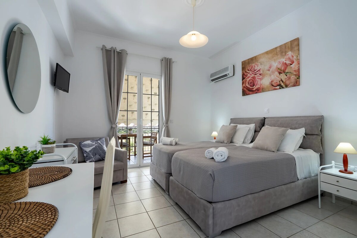 A modern bedroom with a large bed, bedside lamps, a flat-screen TV, and a balcony with a view.