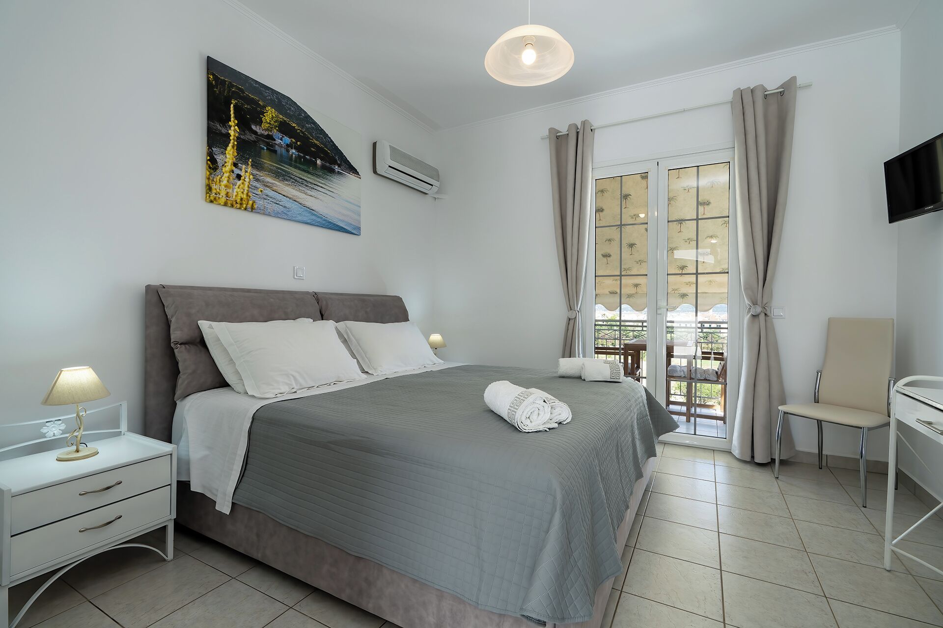 Un dormitorio con cama, mesitas de noche, escritorio, silla, televisor y ventana con cortinas.