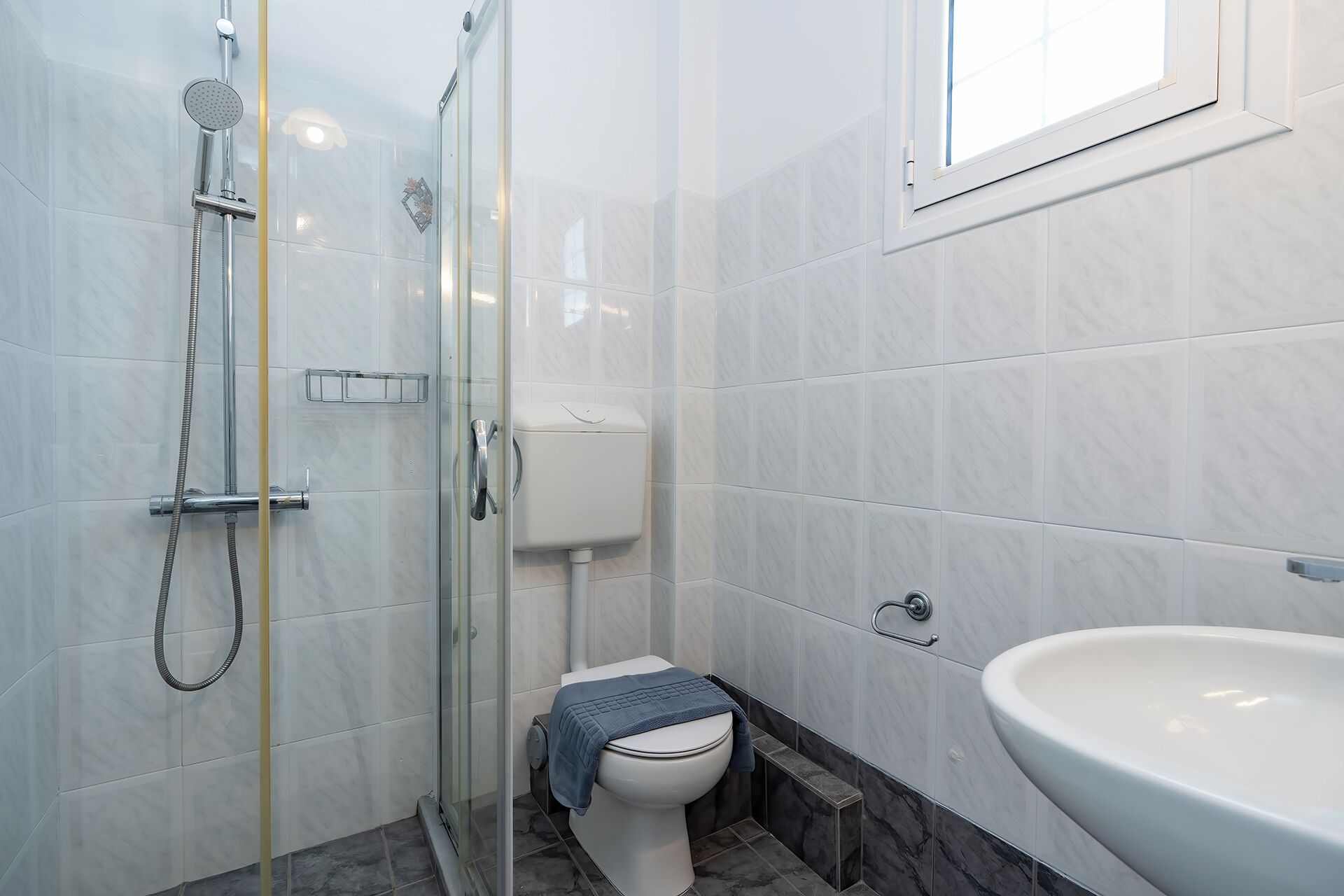 A bathroom with a glass shower enclosure, a toilet, and a sink.