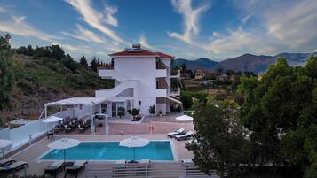 Un hotel moderno con piscina, asientos al aire libre y vistas de las colinas circundantes.