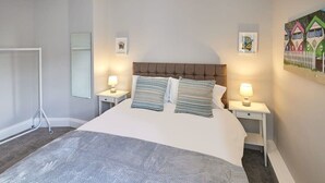 Un dormitorio ordenado con una cama grande, dos mesitas de noche con lámparas, un espejo y un cuadro enmarcado en la pared.