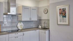 A modern kitchen with white cabinets, a stainless steel range hood, a sink, and a clock on the wall. - Host & Stay | The Glaisdale (Whitby)