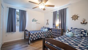 Una habitación con dos camas, ventilador de techo y decoración náutica.