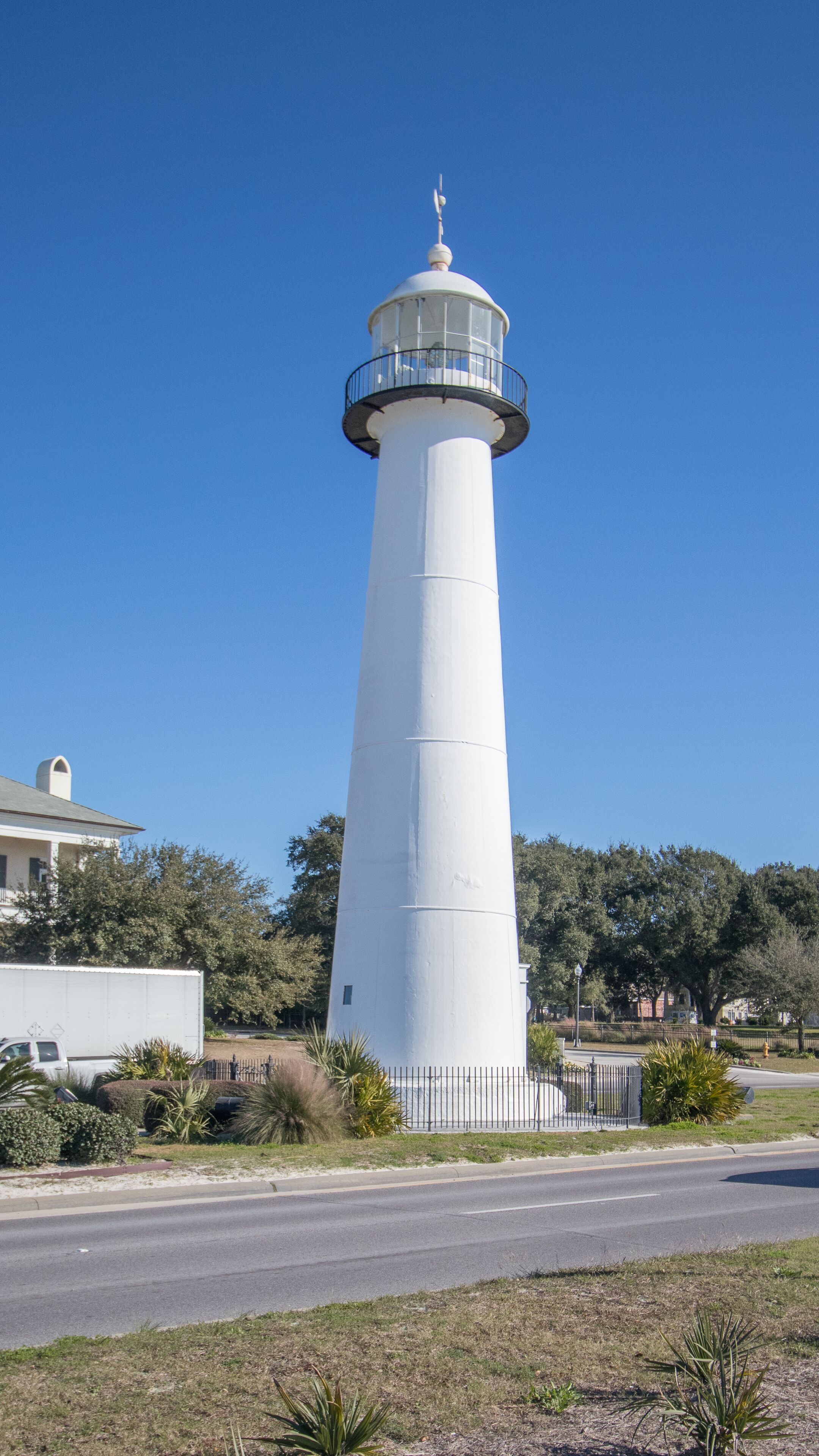 Un grand phare blanc, doté d’une plateforme d’observation circulaire, entouré d’une clôture métallique et de verdure.