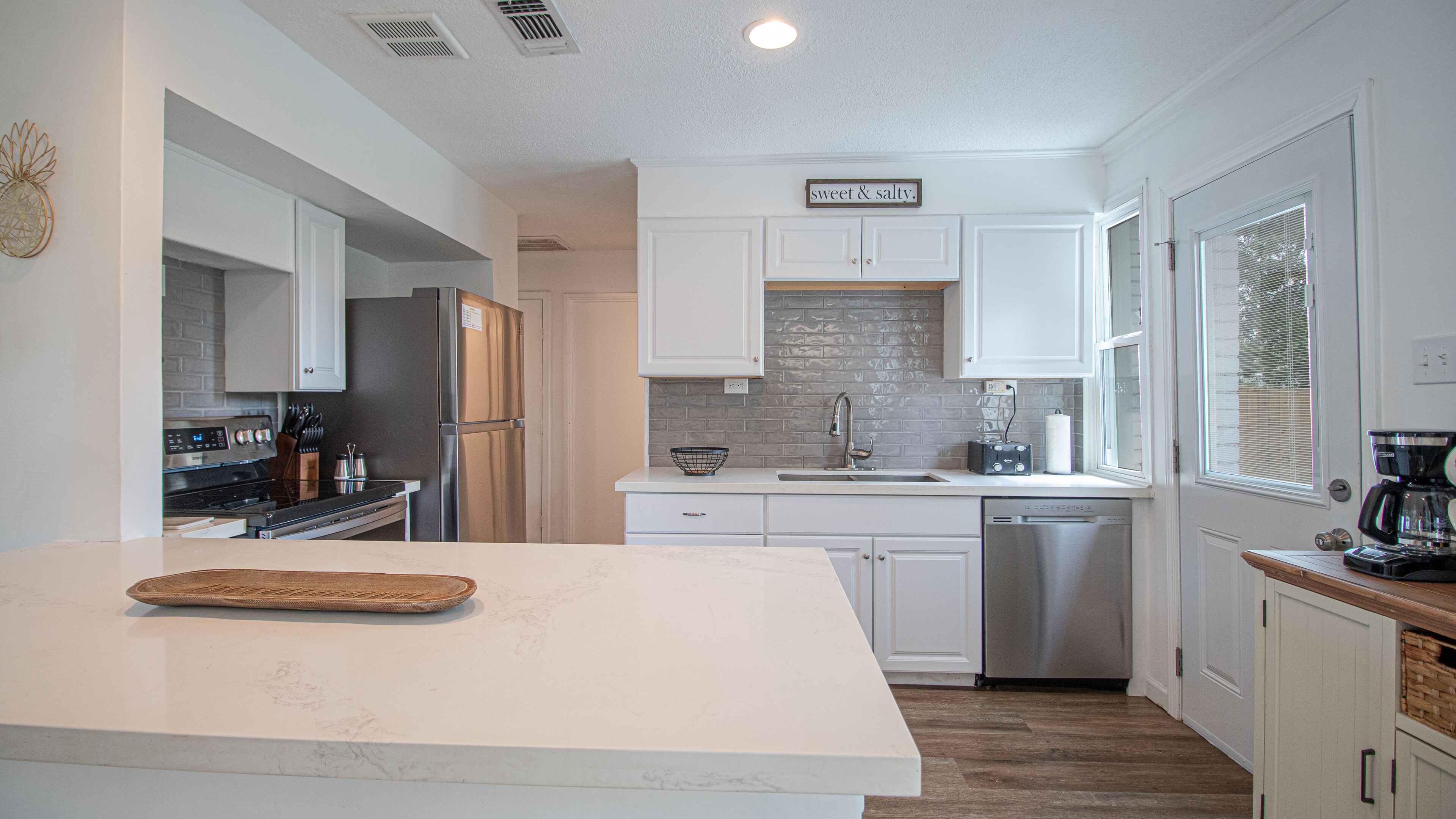 A modern kitchen with white cabinetry, a stainless steel refrigerator, a dishwasher, and a coffee maker.