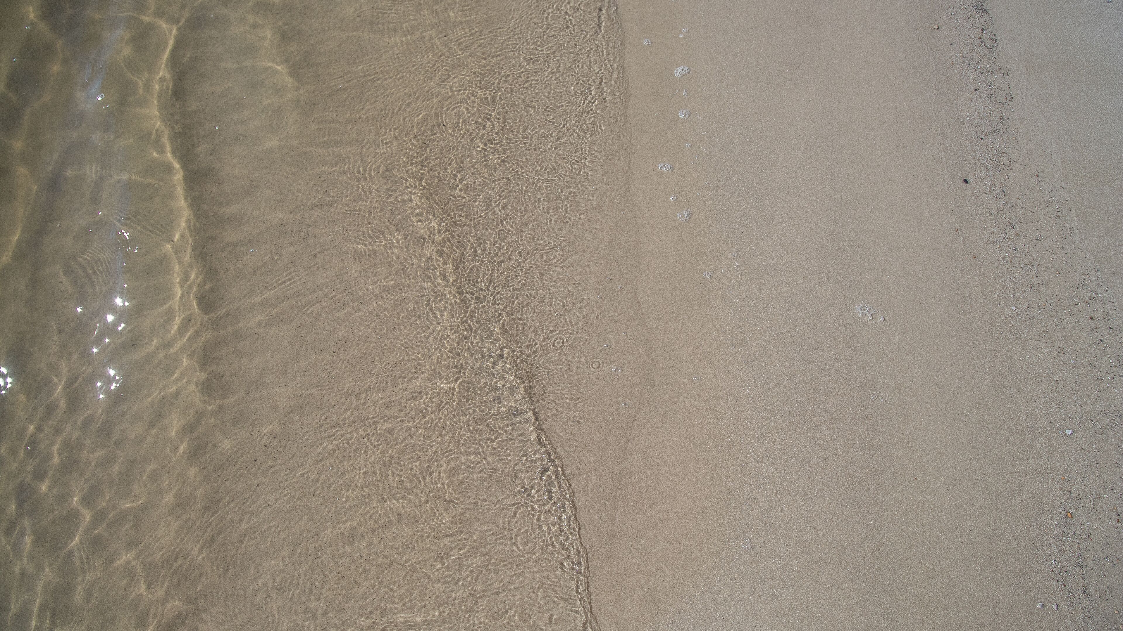 Een zandstrand met helder water en voetafdrukken.