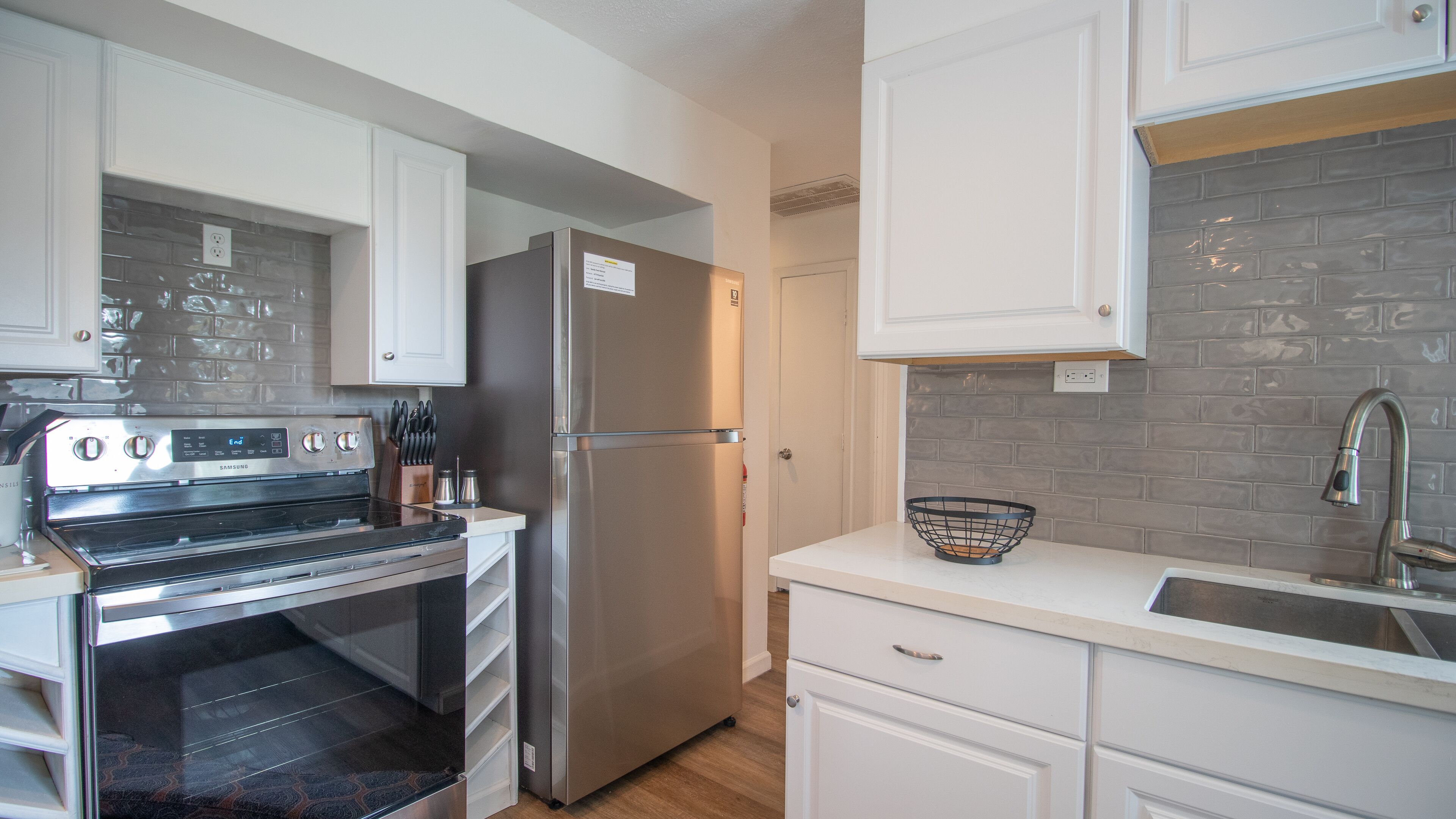 A modern kitchen with white cabinets, stainless steel appliances, and a grey brick backsplash.