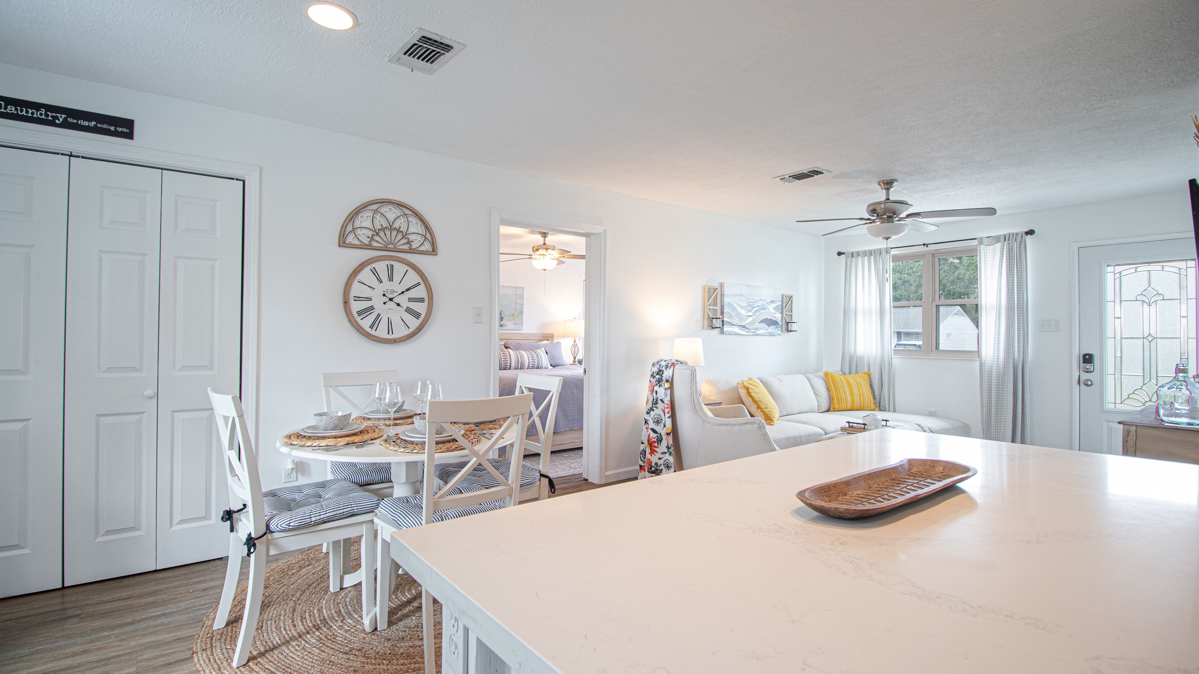 A bright, well-lit room with a dining area, a sofa, and a kitchen counter.