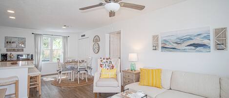 Un salon bien éclairé, doté d’un ventilateur de plafond, d’un canapé, d’une table basse et d’un coin repas avec des chaises et une table.