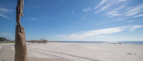 A beach with a wooden sculpture, a paved walkway, and a distant view of the ocean.