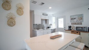 Una cocina con armarios blancos, una isla central y un cuadro decorativo de piñas.