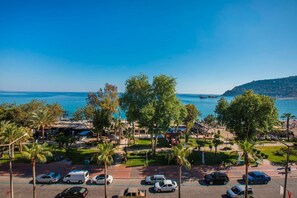 A coastal view with a parking area, palm trees, and a clear blue sky. - Barhan Hotel (Alanya)