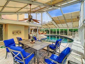 Un área de piscina interior con techo de vidrio, sillas azules y una mesa con planta en maceta.