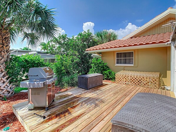 Un patio con una parrilla, mobiliario exterior y una terraza de madera.