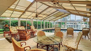 A spacious sunroom with a glass ceiling, wicker furniture, a central glass table, and a view of the outdoors. - Waterfront  (Clearwater)