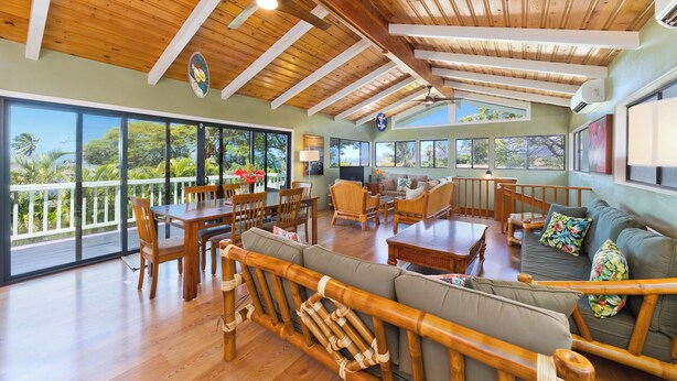 A spacious living area with wooden furniture, large windows, and a balcony. - Large Home in Waikoloa Village | 5-Bedrooms | Newly Updated with AC (Waikoloa)
