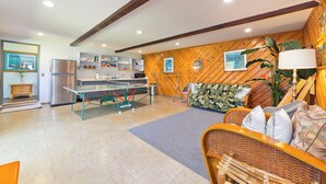 A modern kitchen with a stainless steel refrigerator, a dining table, and a kitchen island. There is a wicker sofa and a lamp in the living area. - Large Home in Waikoloa Village | 5-Bedrooms | Newly Updated with AC (Waikoloa)