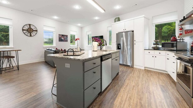 A modern kitchen with a central island, white cabinetry, stainless steel appliances, and a view of greenery outside. - Razorblock South - 1 mi from DT - 3 blocks to UofA (Fayetteville)