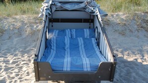 Una cama portátil sobre arena, con una manta a rayas, un dosel y una cuerda.