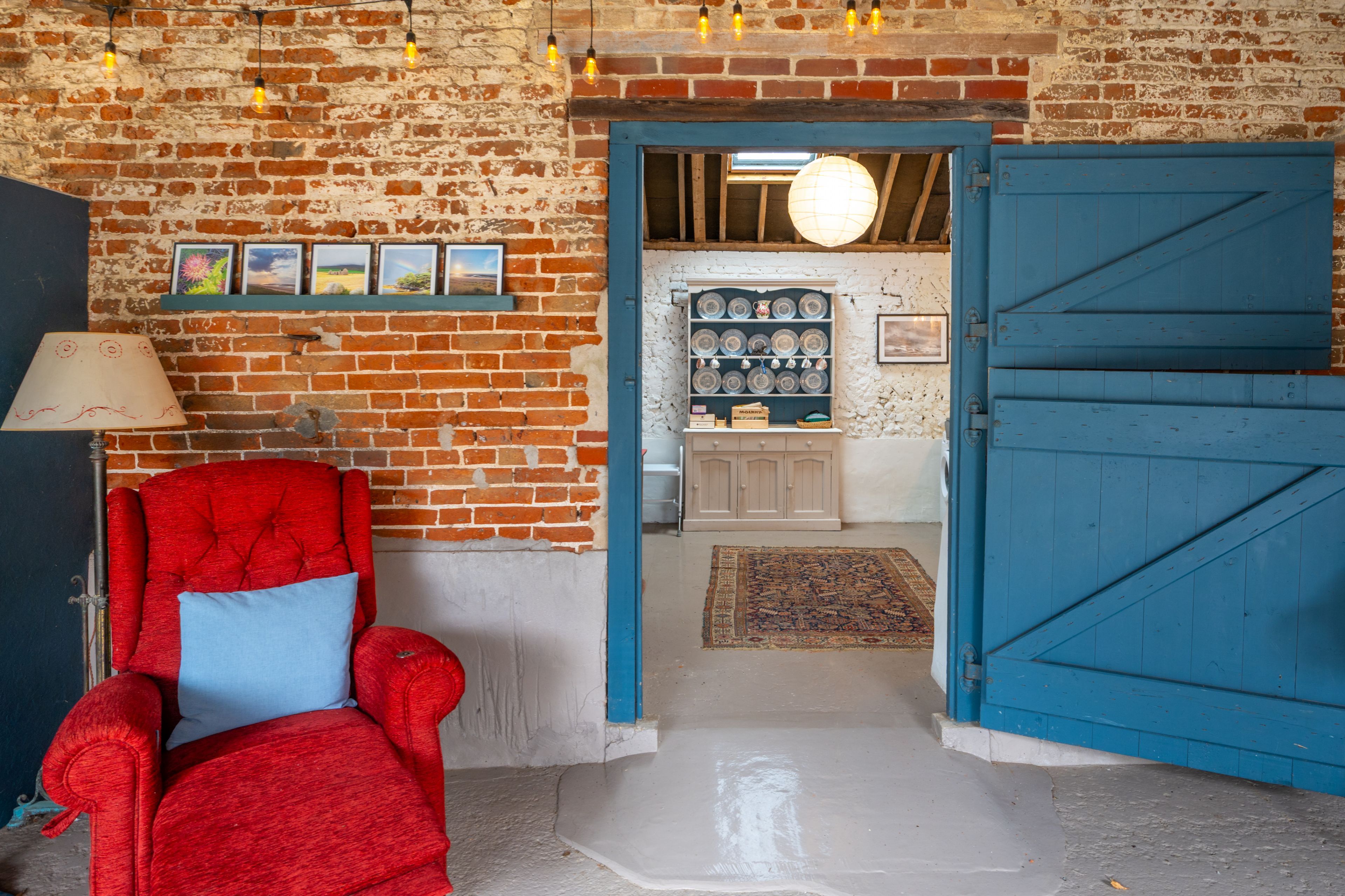 A room with a red armchair, a blue door, and a brick wall with pictures.