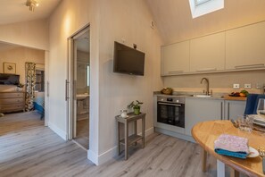 A modern kitchen with a built-in oven, a dining area with a wooden table, and a small side table with a candle. - The Able Stables - Sam's Cottage, East Rudham, Norfolk (East Rudham)