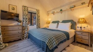 A bedroom with a bed, two bedside tables, a TV, a window with curtains, and a shelf above the bed. - The Able Stables - Sam's Cottage, East Rudham, Norfolk (East Rudham)