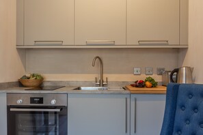 A modern kitchen with stainless steel appliances, a built-in oven, a sink, and a wooden cutting board with vegetables. - The Able Stables - Sam's Cottage, East Rudham, Norfolk (East Rudham)
